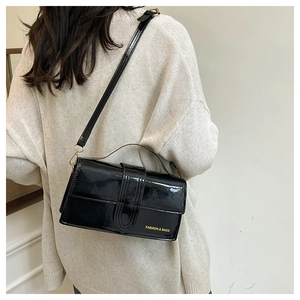 Detail of black patent leather crossbody bag with gold lettering and glossy mirror finish