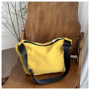 Detail of yellow nylon crossbody bag with adjustable black strap on a wooden chair