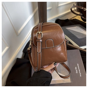 Détail du sac bandoulière en cuir marron brillant avec coutures blanches et dorure