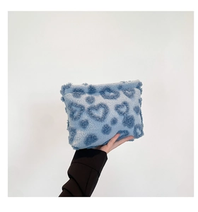 Detail of light blue fuzzy clutch bag with dark blue heart patterns and soft texture