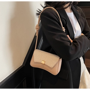 Gros plan d'un sac bandoulière beige carré avec boucle dorée sur un blazer noir élégant