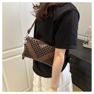 Detail of brown leather crossbody bag with black rivets in V-shape arrangement