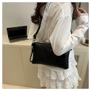 Detail view of black leather crossbody bag with V-shaped matte studs on a female model