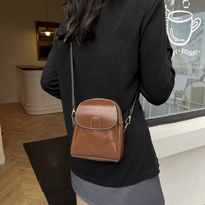 Sac à bandoulière marron caramel en similicuir brillant porté par un modèle dans un décor urbain