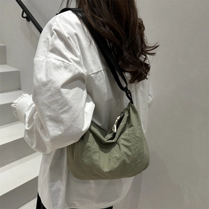 Unisex olive nylon crossbody crescent bag shown on a model in a minimalist outdoor setting
