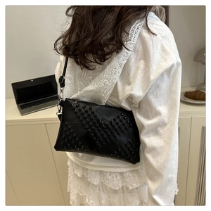 Detail of black leather crossbody bag with V-shaped stud patterns and slim strap