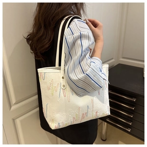 Detail of white textured tote bag with colorful embroidery and gold metallic hardware accents