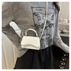 Detailed view of white patent leather mini crossbody bag with unique wavy flap and top handle