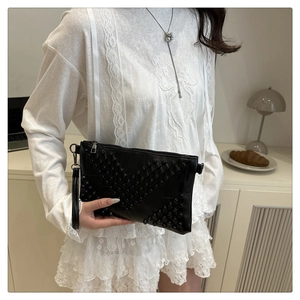 Detail of black leather clutch bag with V-shaped rivet pattern and wrist strap
