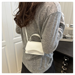 Detailed back view of white patent leather mini bag worn with adjustable crossbody strap