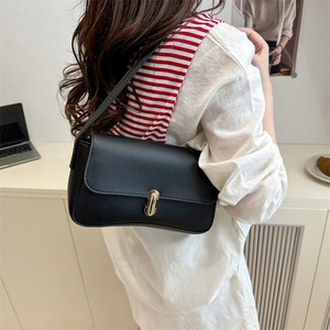 Chic black leather minimalist shoulder bag with gold clasp shown on a female model