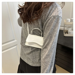 Detailed view of mini white patent leather shoulder bag with stylish wavy flap edge
