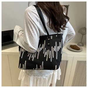 Detail showing colorful wavy embroidery on a black canvas tote bag with leather straps