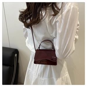 Macro detail of glossy dark wine red patent leather shoulder bag on a model