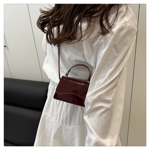 Close-up of wine red patent leather mini crossbody bag styled on a white dress