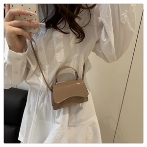 Close-up of beige glossy mini crossbody bag with a wavy flap and slender shoulder strap