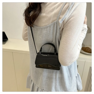 Detail view of a black patent leather mini shoulder bag with elegant curved bottom lines
