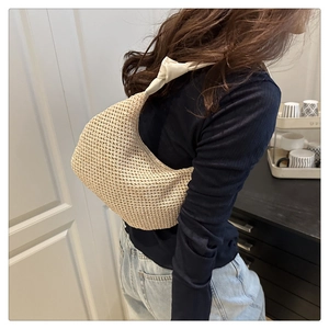 Shoulder shot of a beige crescent knit bag featuring a unique knotted strap and texture