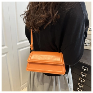 Detail of bright orange square crossbody bag with adjustable strap worn on person