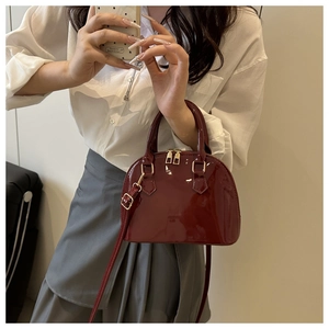 Detail of burgundy patent leather shell bag with gold hardware and adjustable strap