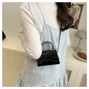Detail shot of a black patent leather mini crossbody bag styled with a summer outfit