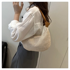Detail of hand-woven straw underarm bag with brown knotted strap on a model