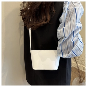 Detailed view of white minimalist bucket bag with FANYISSA embossing worn by model