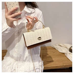 Detail of woven straw handbag with brown leather base and gold metal circular handle
