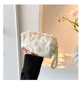 Close-up of white plush handbag with floral texture and bright green ring handle