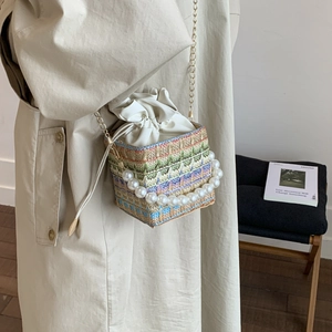 Fashionable woven bucket bag with pearl handle and metal chain shown on model in studio