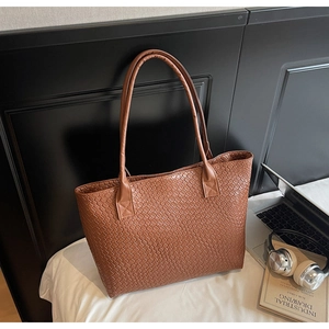 Gros plan du sac cabas en cuir tressé marron avec de longues anses dans un décor moderne