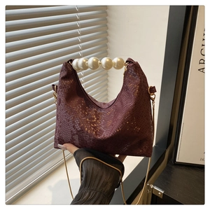 Detail of burgundy snakeskin texture handbag with large pearl handle and gold chain strap