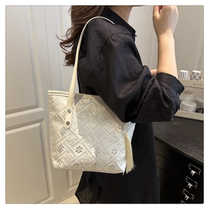 Detail of cream tote bag with geometric embossed pattern and silk tassel charm