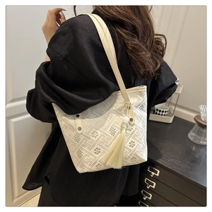 Detail of embroidered tote bag with geometric patterns and tassels on model shoulder