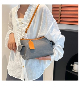 Detail of grey denim shoulder bag with brown leather trim and adjustable strap on a model