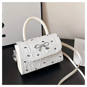 Détail d'un sac bandoulière blanc avec imprimé nœuds noirs et texture plissée chic