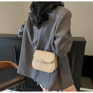 Detail of beige mini crossbody bag with silver heart buckle and gold chain strap