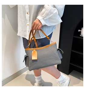Detail of grey textured handbag with orange leather trim and adjustable shoulder strap