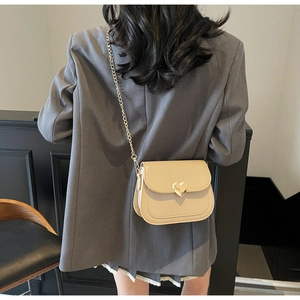 Beige faux leather crossbody bag with gold heart buckle shown on a model's back