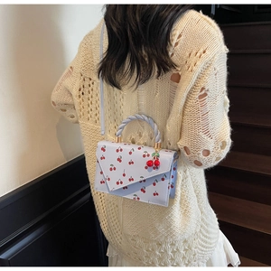 Detail of light blue cherry print square bag with woven handle and 3D cherry charm