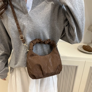 Brown ruched dumpling shoulder bag with gold chain strap held by model in minimalist setting
