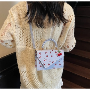 Light blue crossbody bag with cherry prints and woven handle shown on a model