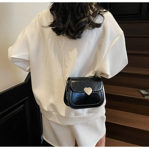Chic black crossbody bag with gold heart clasp and chain strap shown on model's outfit