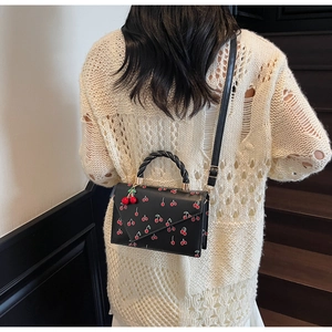 Detail of black cherry print crossbody bag worn by a model against a minimalist wall