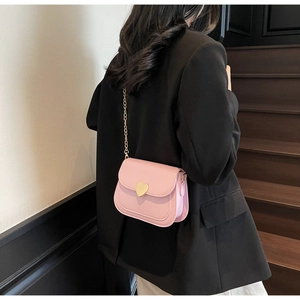 Pink crossbody bag with gold heart clasp and chain strap shown on a black blazer