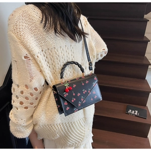 Detail of black cherry print leather crossbody bag with 3D cherry pendant on model