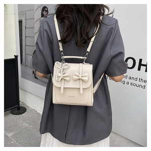 Detail of cream backpack featuring 3D bows and pearl butterfly charm with fashion text