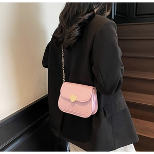 Pink mini crossbody bag with golden heart clasp shown on a model's shoulder side view