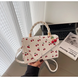 Detail of white leather handbag with cherry print, woven handle, and cherry charm