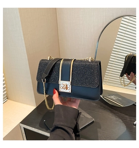 Close-up of stylish black glitter patchwork shoulder bag with golden metallic twist lock